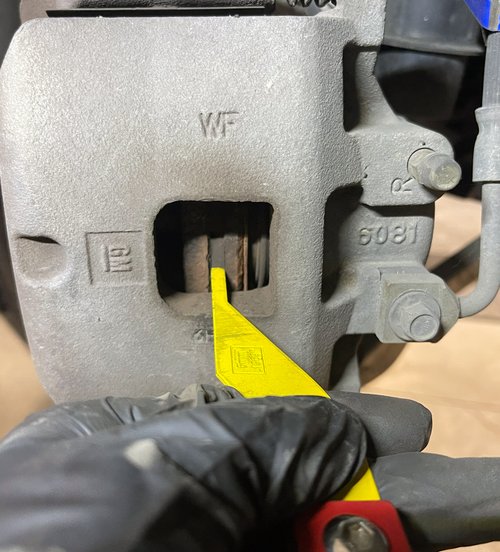 measuring brake pad thickness with a gauge during an inspection at Tizzano Automotive