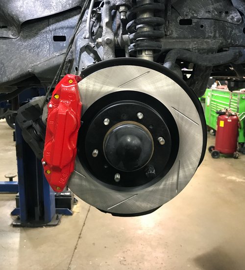 slotted brake rotor and red caliper on a lifted vehicle at Tizzano Automotive in Plain City, OH